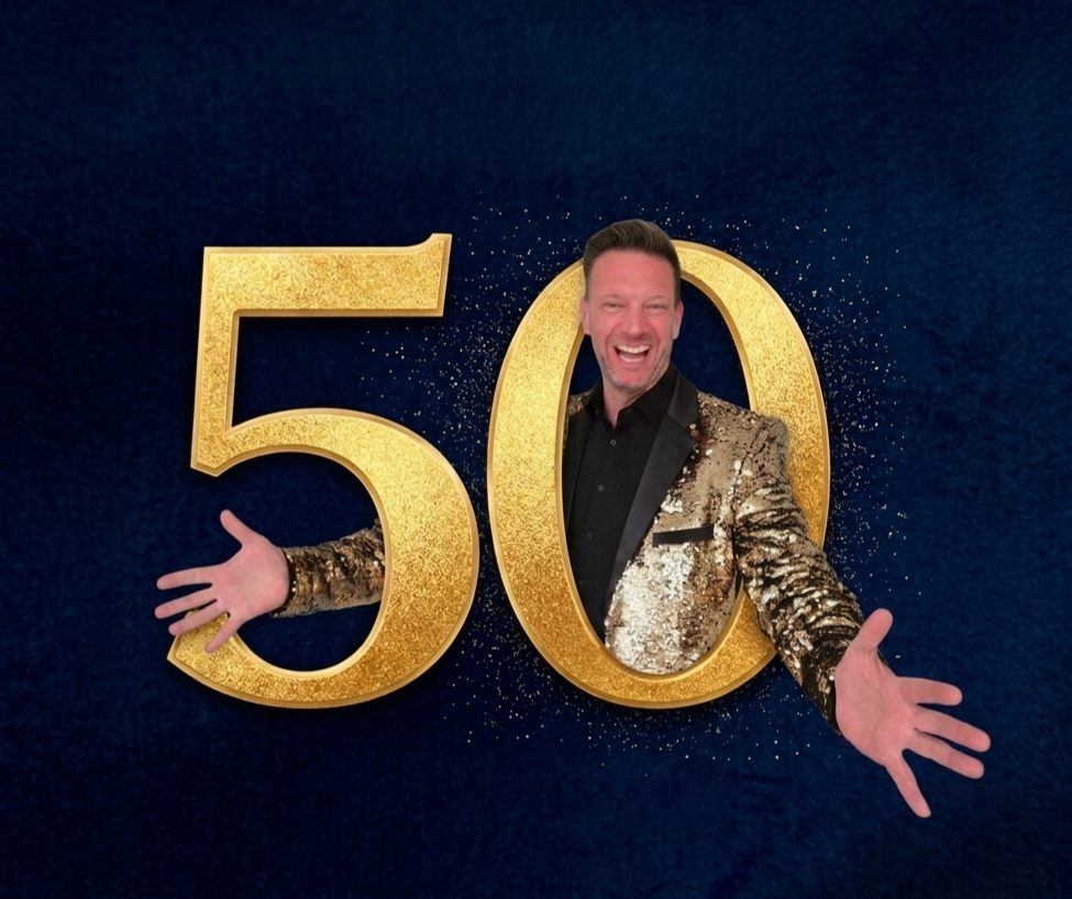 Jeroen Schellekens in glitterjasje met wijd uitgespreide armen achter een gouden 50